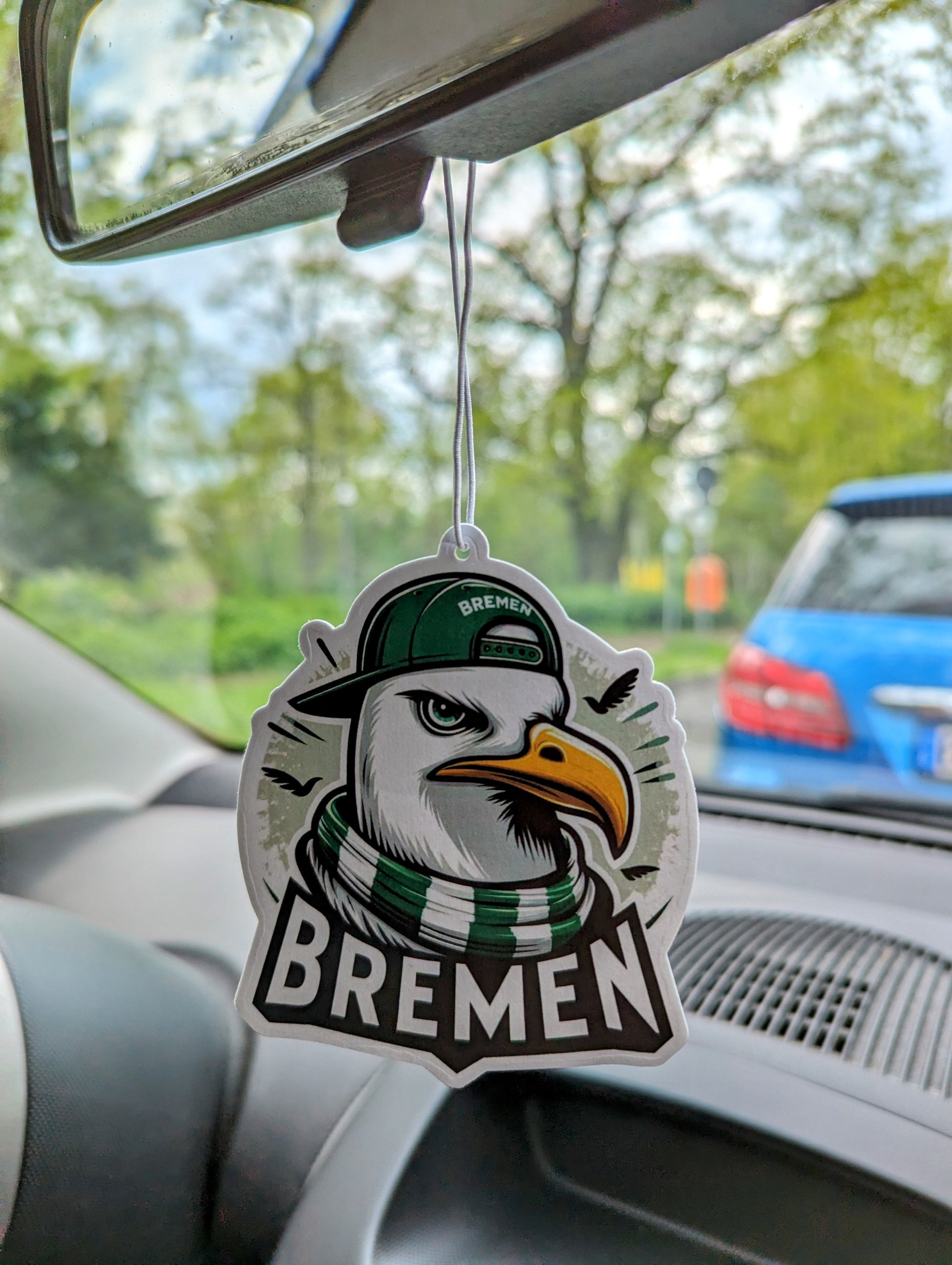 Auto Duftbaum Bremen Möwe mit grün und weißem Schal, dazu eine grüne Basecap, hängt am Auto Rückspiegel