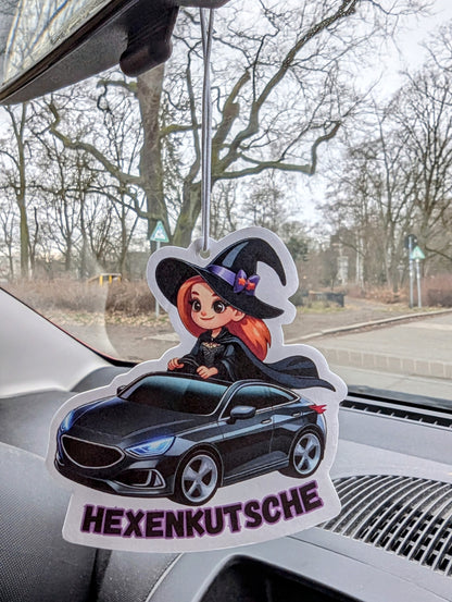 Auto Duftbaum mit Comic-Hexe in schwarzem Kleid und spitzem Hut, die ein schwarzes Auto fährt, Schriftzug „Hexenkutsche“ darunter, Lufterfrischer fürs Auto mit witzigem Motiv als originelle Geschenkidee.