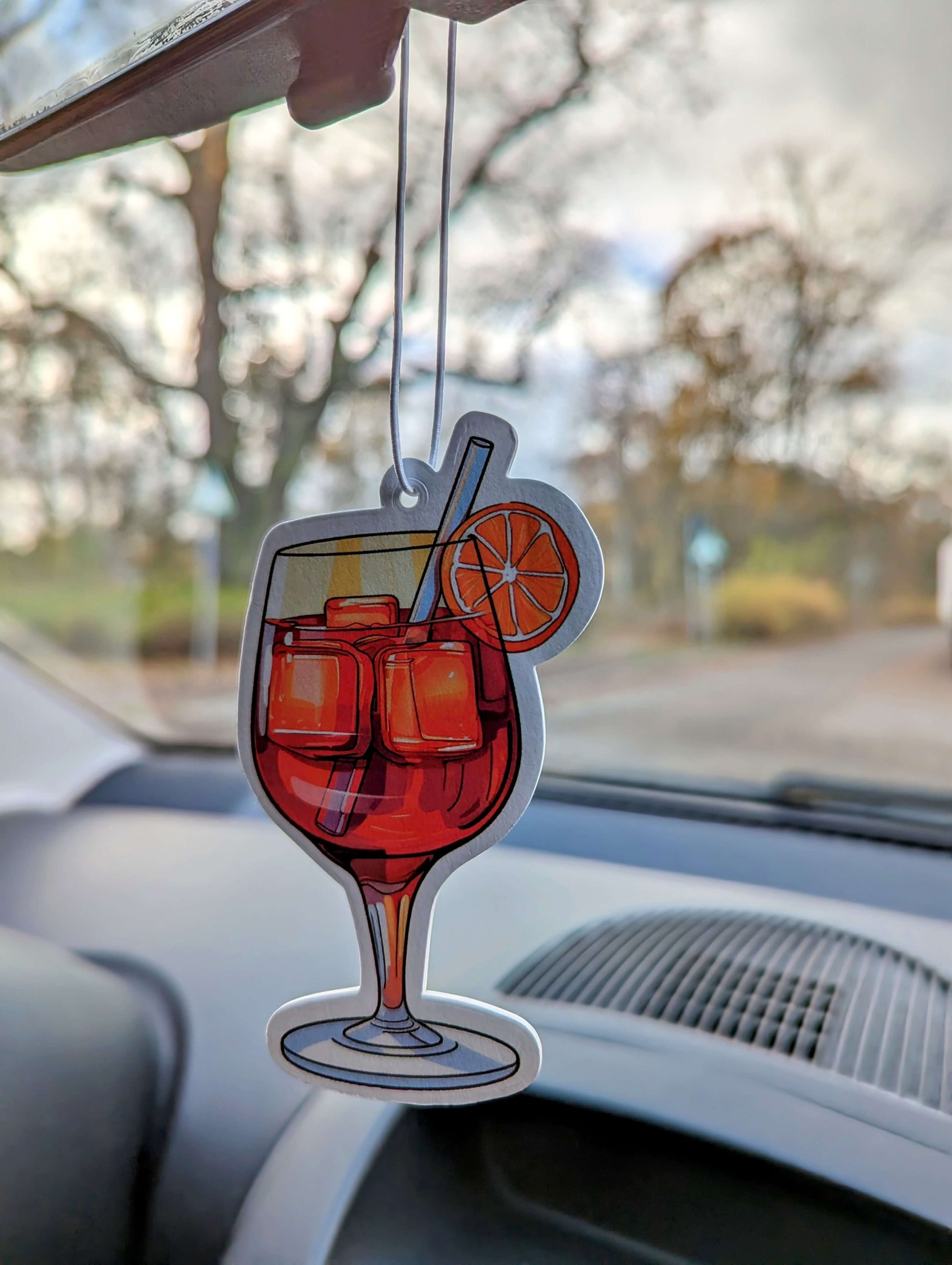 Auto Duftbaum Spritzo Aperetif mit einem Strohhalm und einer Orangen-scheibe hängt am Auto Rückspiegel