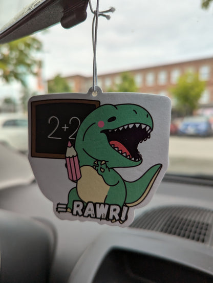 Auto Duftbaum T-Rex, zeigt auf eine Tafel und hängt im Auto am Rückspiegel