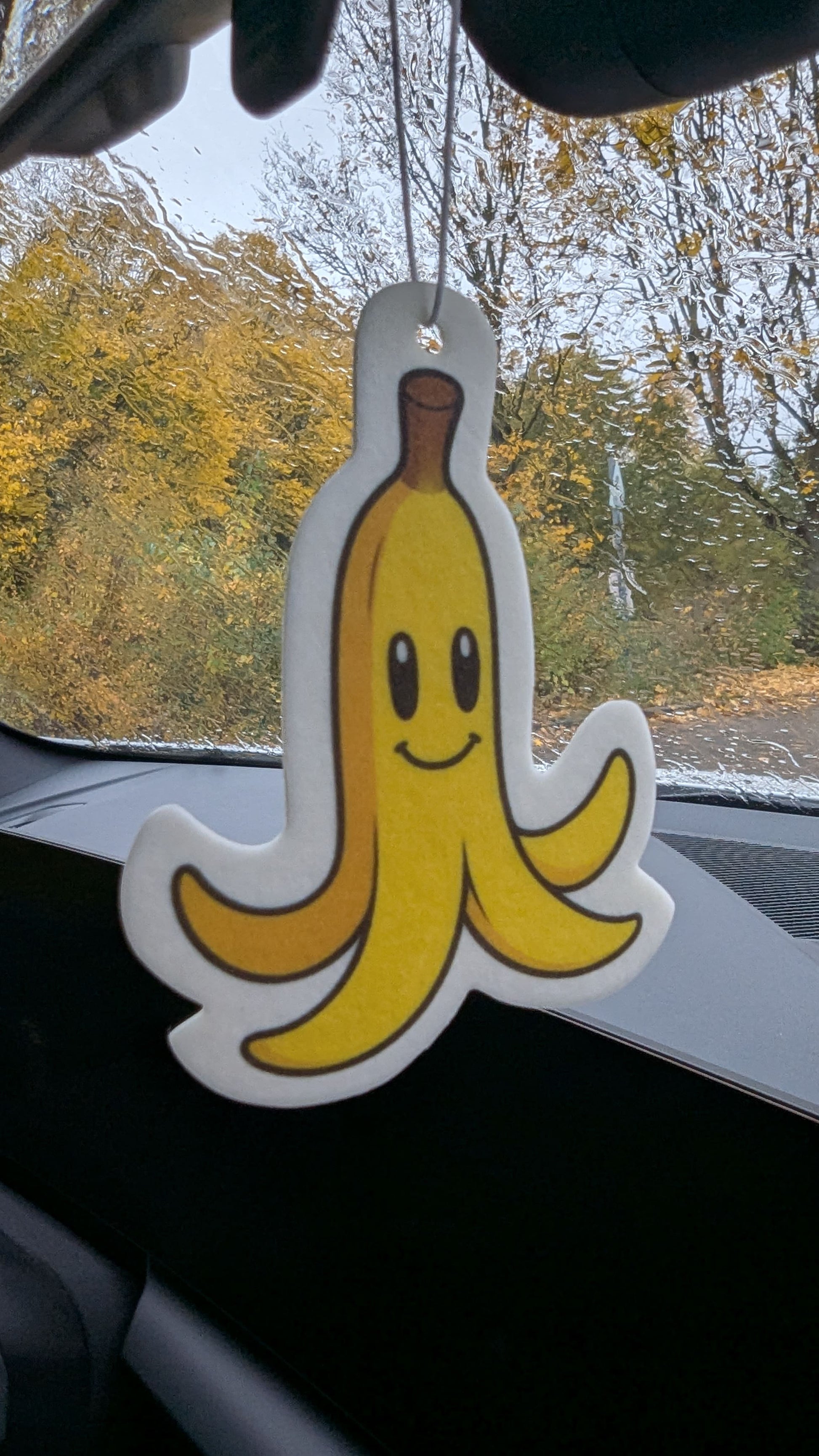 Gelbe Bananenschale mit Gesicht als lustiger Auto Duftbaum und Lufterfrischer am Rückspiegel aufgehängt